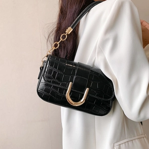 Black crocodile pattern shoulder bag with gold chain strap worn by model in white blazer
