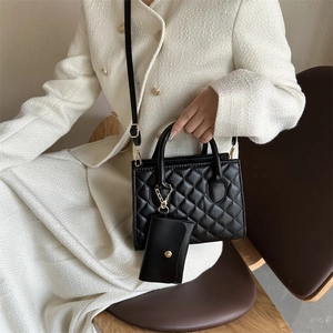 Chic black quilted handbag with gold hardware and small pouch on a white tweed coat