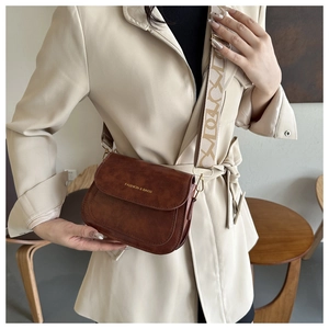 Détail d'un sac besace marron vintage avec bandoulière à motifs sur un manteau beige