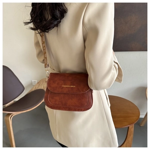 Détail du sac besace vintage en cuir marron avec logo et bandoulière en tissu imprimé