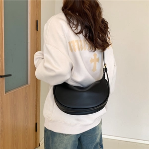 Minimalist black leather half-moon shoulder bag shown from a model's back perspective