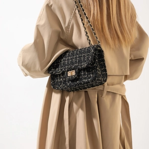 Classic black tweed shoulder bag with gold chain strap shown on model in beige coat