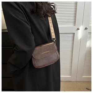 Détail de la besace marron avec lettrage doré et large bandoulière en jacquard