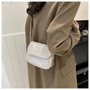 Détail d'un sac bandoulière beige avec texture marbrée porté par un mannequin