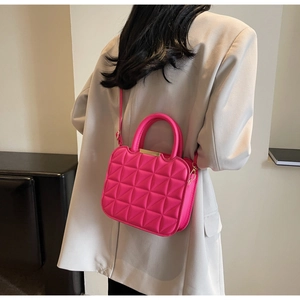 Detailed close-up of rose red quilted crossbody bag with metal trim and top handles