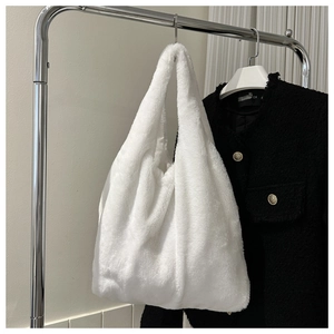 Détail d'un cabas en peluche blanc suspendu sur un cintre avec une veste noire en fond