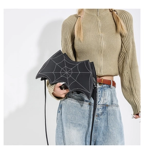 Detail of bat-shaped crossbody bag featuring white spider web stitching on black leather