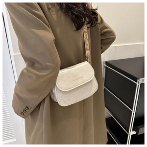 Détail du sac besace crème avec large bandoulière lettrée porté sur un manteau marron