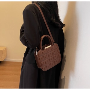Detail of dark brown quilted handbag showing round handle and gold metal trim in use