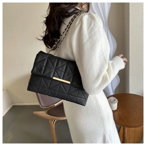 Détail du sac à bandoulière matelassé noir avec boucle dorée porté sur une tenue