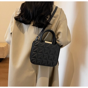 Close-up of a black quilted handbag with fine stitching and gold hardware on a beige coat
