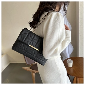Détail d'un sac bandoulière noir matelassé avec chaîne dorée porté par une femme