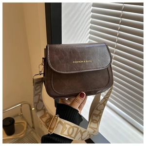 Détail du sac selle en cuir marron vintage avec logo et bandoulière tissée large