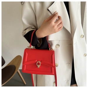 Detail of red textured handbag with gold hardware clasp on a white coat model