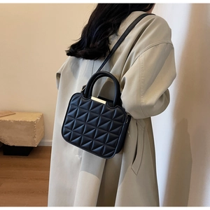 Detail of a black quilted shoulder bag with triangular stitching and gold metal bar accent