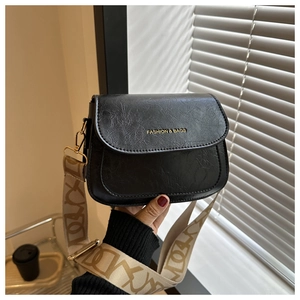 Détail du sac selle noir texturé avec lettrage doré et bandoulière jacquard à motifs