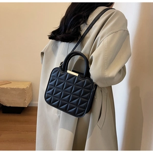 Detail of a black quilted crossbody bag with golden metal hardware on a beige coat