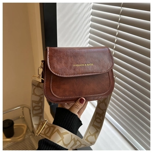 Détail d'un sac bandoulière vintage marron avec large sangle géométrique et logo doré brillant