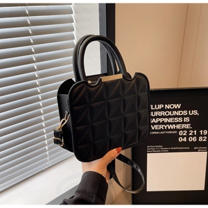 Detail of black quilted texture on handbag with gold metal clasp and dual top handles