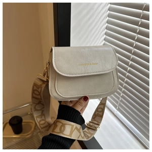 Détail du sac selle beige avec large bandoulière à motifs et inscription dorée