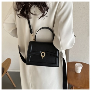 Detail view of black faux leather handbag featuring a vintage square box design and gold buckle