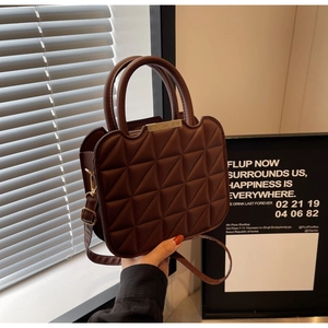 Detail of dark brown quilted handbag with dual round handles and gold metallic hardware