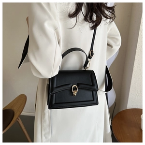 Classic black flap handbag with gold metal clasp shown on a model in a cozy interior
