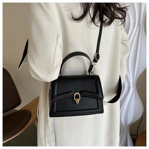 Detail of black leather handbag featuring golden metal buckle and decorative stitching