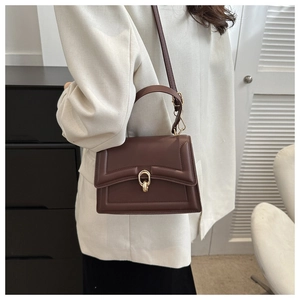 Brown leather handbag with gold oval buckle shown as a crossbody on a female model
