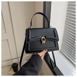 Detail of minimalist black matte leather handbag featuring a unique gold double-ring clasp