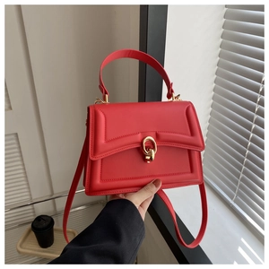 Detail of red faux leather handbag featuring a golden circular twist lock and matte finish