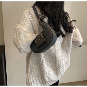 Détail du sac demi-lune noir avec boucle dorée sur un pull en maille blanche texturée