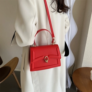 Chic red leather handbag with gold ring buckle and crossbody strap in a minimalist setting