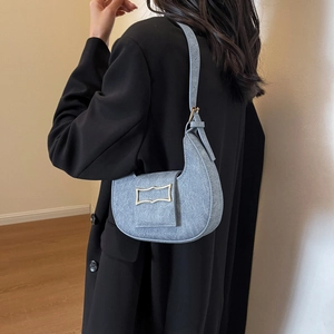 Sac croissant en denim bleu rétro avec boucle dorée porté sur un blazer noir chic