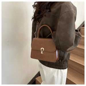 Detail of vintage brown PU leather handbag with golden U-shaped clasp on elegant model