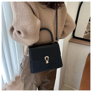 Detail of elegant black square bag with golden horseshoe buckle on stylish knit outfit