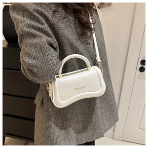 Macro detail of white curved faux leather handbag with golden hardware and Fashion text