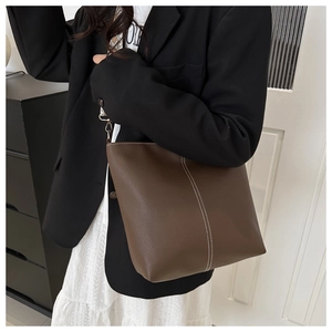 Close-up of brown pebbled leather bucket bag with white contrast stitching and jacquard strap