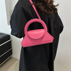 Bright pink geometric handbag with circular top handle and crossbody strap on dark coat