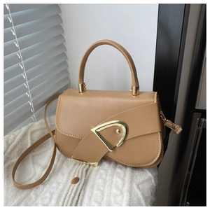 Detail of camel leather saddle bag featuring a large gold D-shaped buckle on a white knit