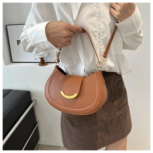 Dettaglio borsa a sella color caramello con fibbia dorata a mezzaluna su abito