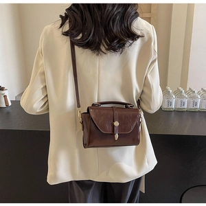 Détail du sac vintage marron foncé avec fermoir doré porté à l'épaule du mannequin