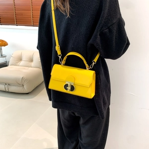 Minimalist yellow leather square crossbody bag with metal T-lock shown on a model