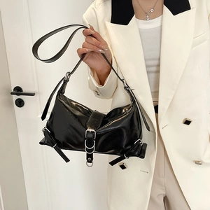Glossy black patent leather shoulder bag with silver buckle worn by a model