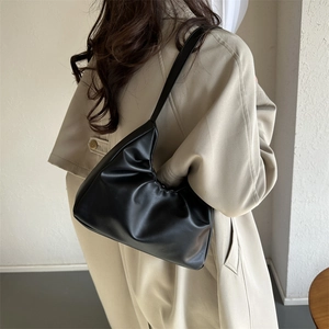 Fashionable black leather pleated crescent shoulder bag shown on model in khaki trench coat