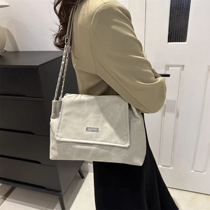 Chic beige tote bag with a chain strap shown on a shoulder in a modern room