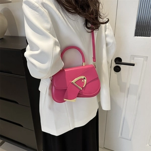 Chic rose pink crossbody bag with a large gold buckle shown on a white blazer outfit