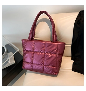 Detail of burgundy quilted puffer tote bag with metallic finish on a cream leather seat