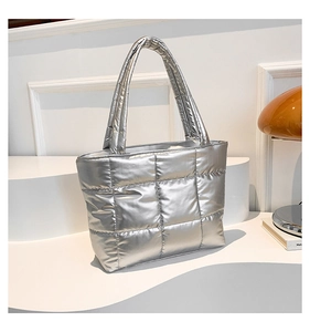Detail view of silver quilted tote bag with metallic finish on a white geometric stand