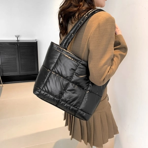 Minimalist black quilted puffer tote bag shown from a side angle on a female model